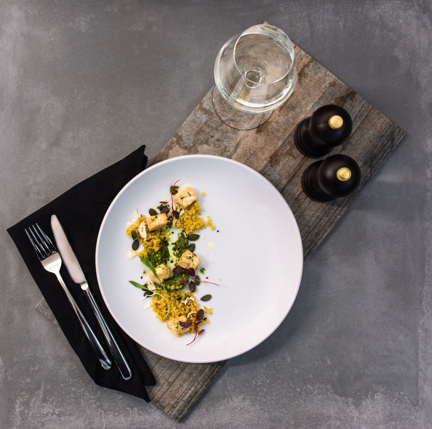 Elegant plated dish with golden saffron rice and garnishes on white plate against dark rustic backdrop with wine glass.