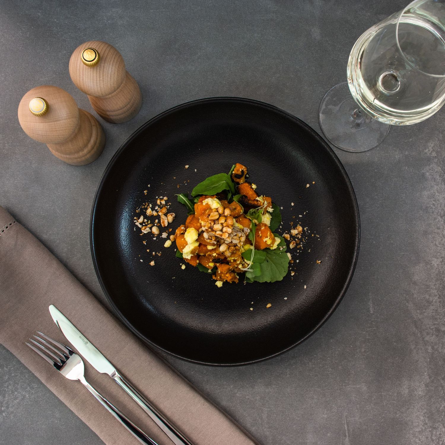 Gourmet dish plated on black ceramic plate with wooden salt and pepper mills.