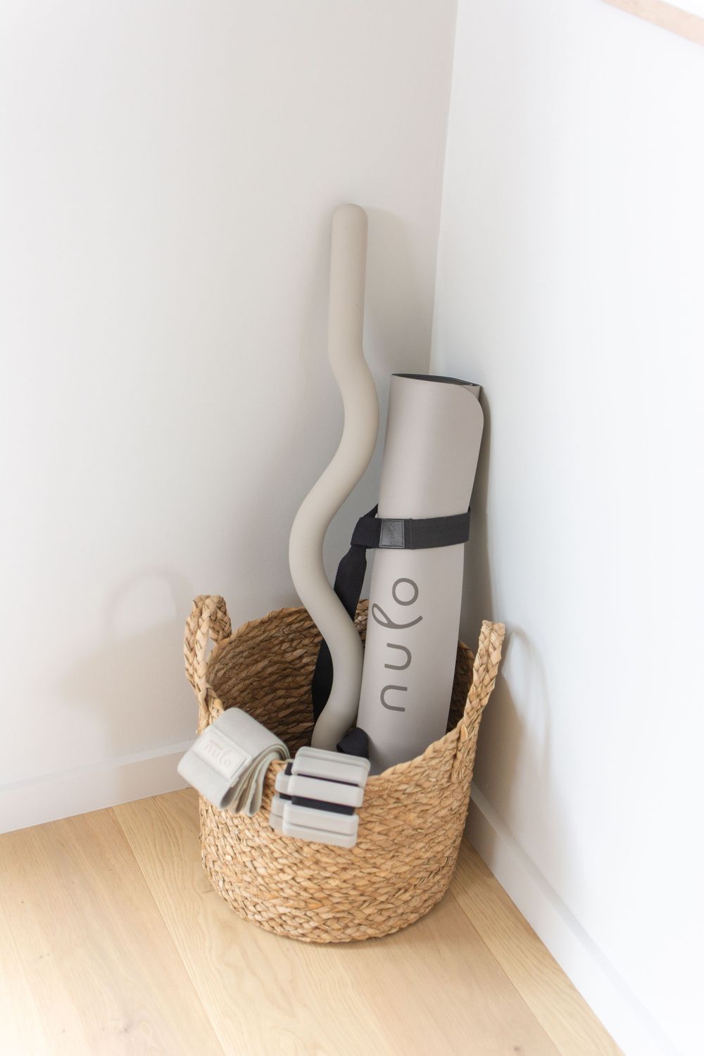 Woven seagrass basket holding a rolled nulo yoga mat and small weights in a bright corner.