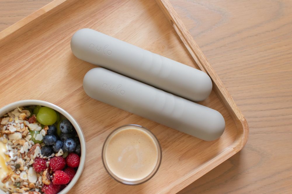 Wooden tray with two hand weights, a bowl of granola with berries, and a small cup of peanut butter.