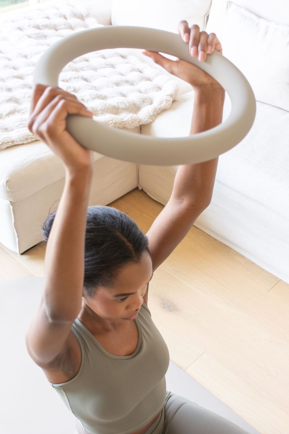 Woman holding a nulo training ring overhead during a home workout session on a hardwood floor.