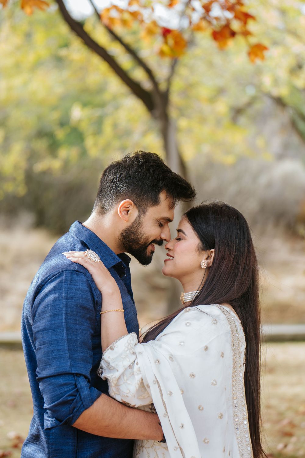 A romantic couple shares tender moments in an autumn park with golden leaves falling from trees in the background.