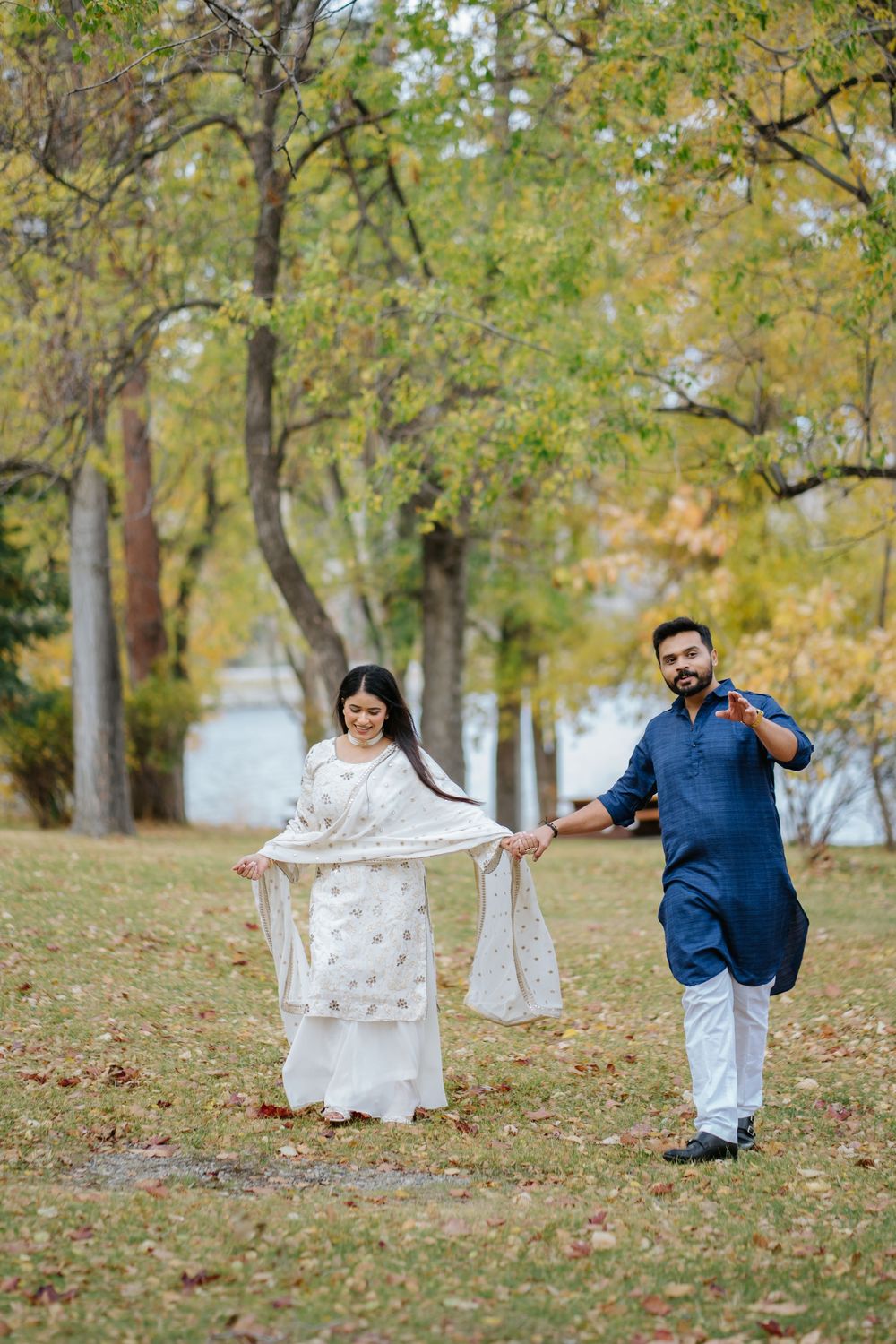 Couple playfully running through autumn trees and fallen leaves in a romantic outdoor photo sequence.