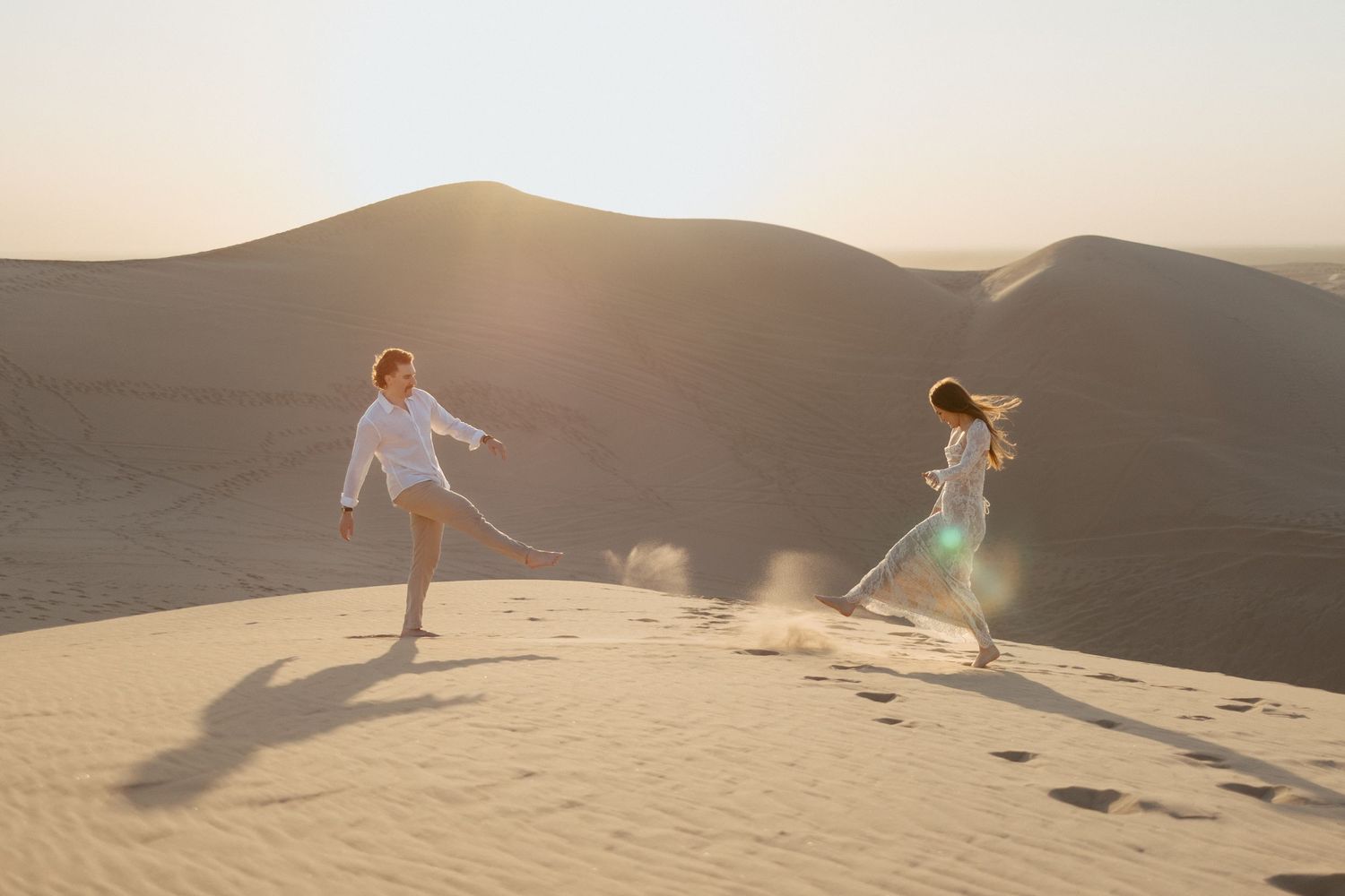 People walk through shallow waters at sunset creating reflective silhouettes against a mountainous backdrop.