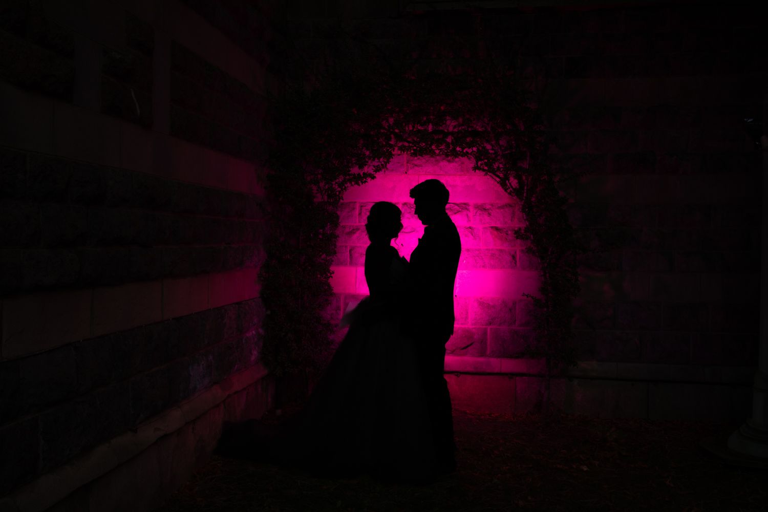 Silhouette of a romantic couple embracing against a vibrant pink backlight in a dark tunnel.