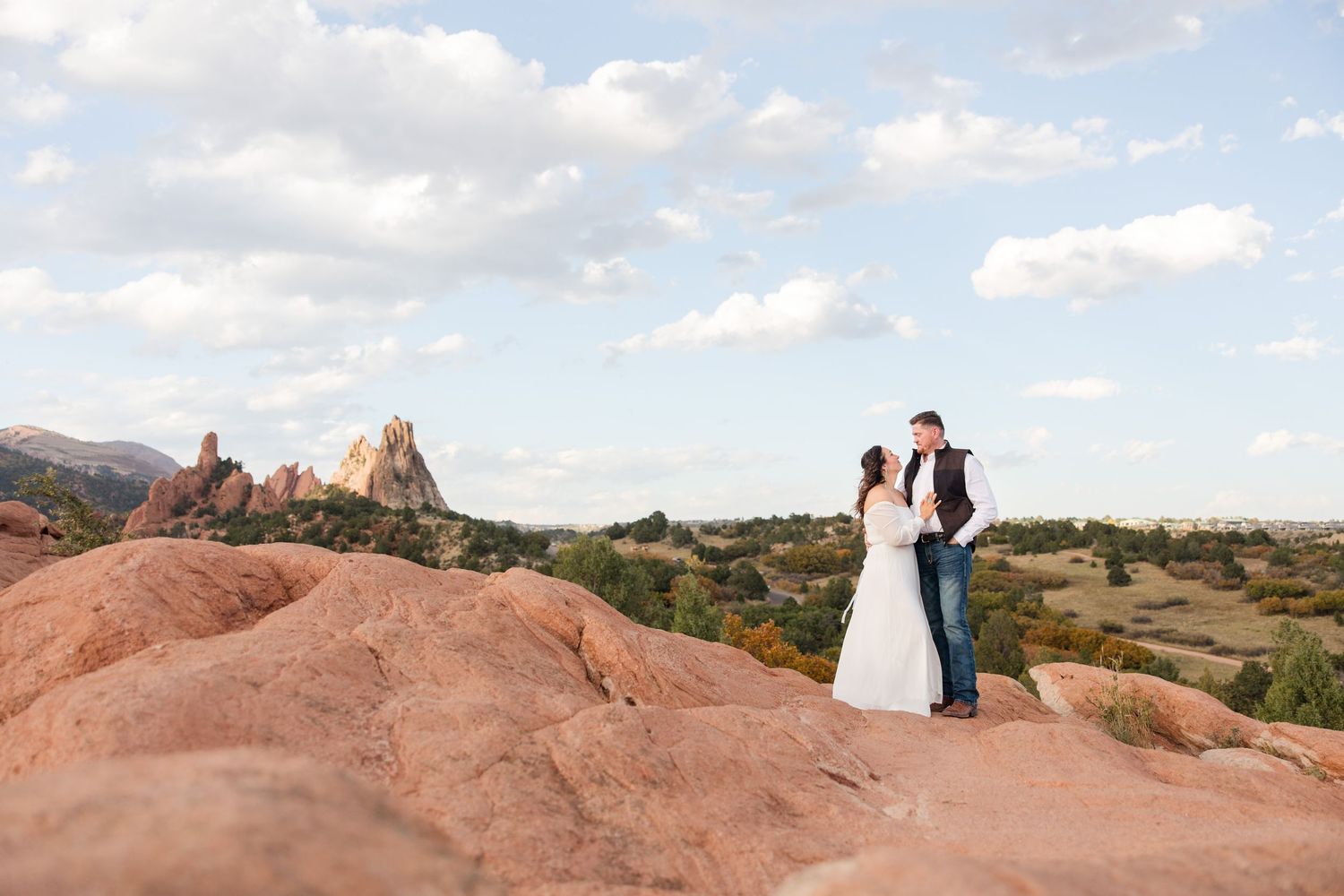 Two figures in formal attire stand on red rock formations at Garden of the Gods during sunset.