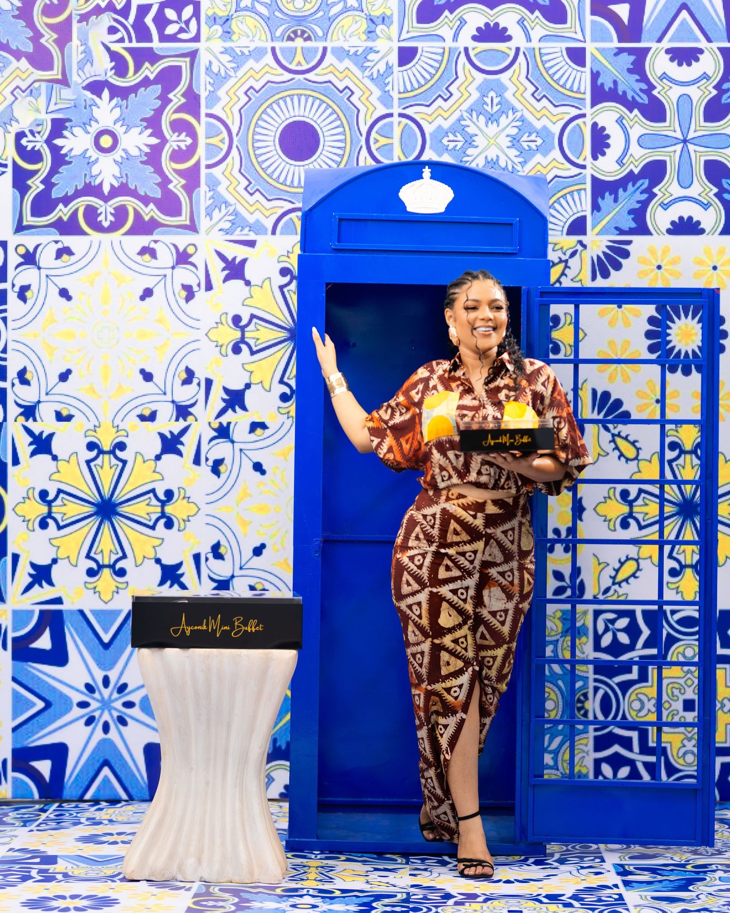 Person in brown pattern dress poses against vibrant blue and white tile wall backdrop.