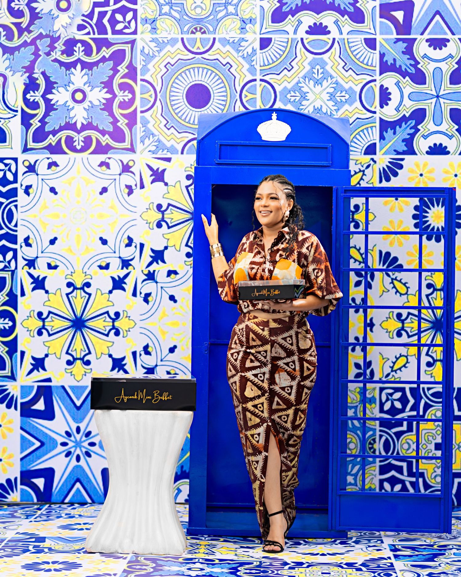 Person in patterned dress poses against blue and white decorative tile backdrop.