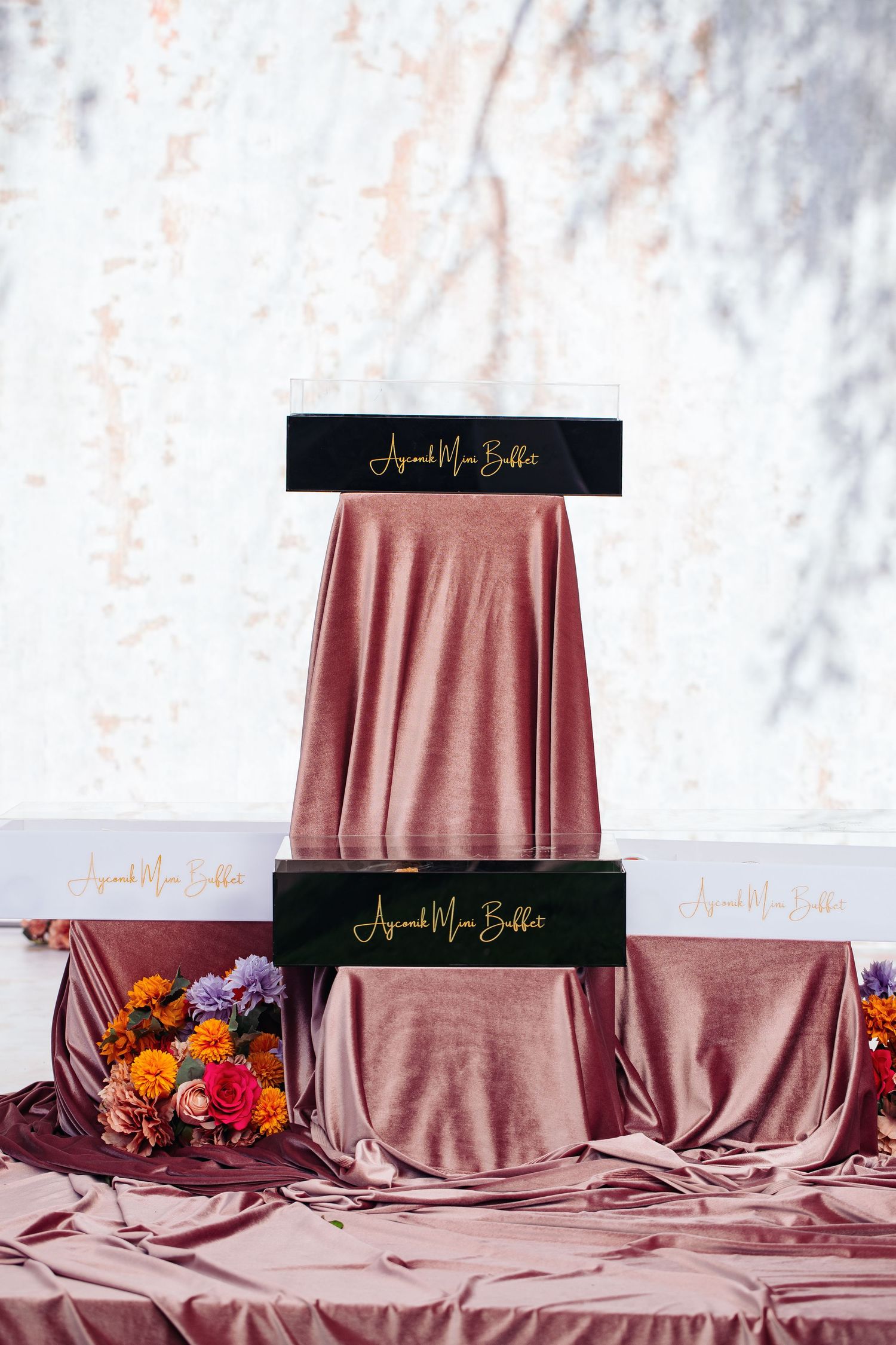 Elegant tiered display setup with dusty rose tablecloth and floral arrangements.