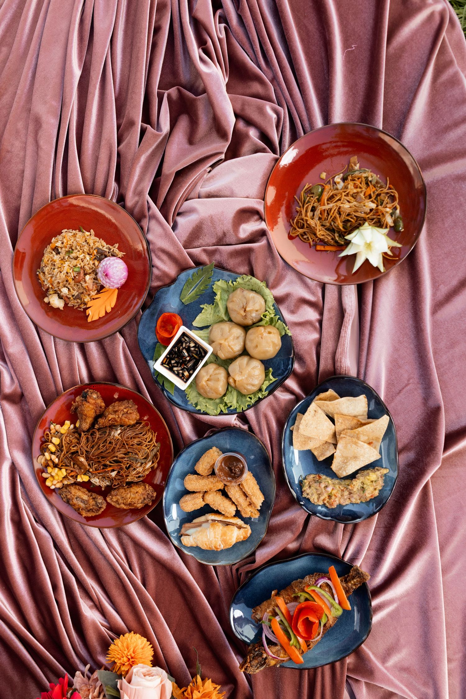 Variety of appetizers and snacks arranged on blue plates over pink satin fabric.