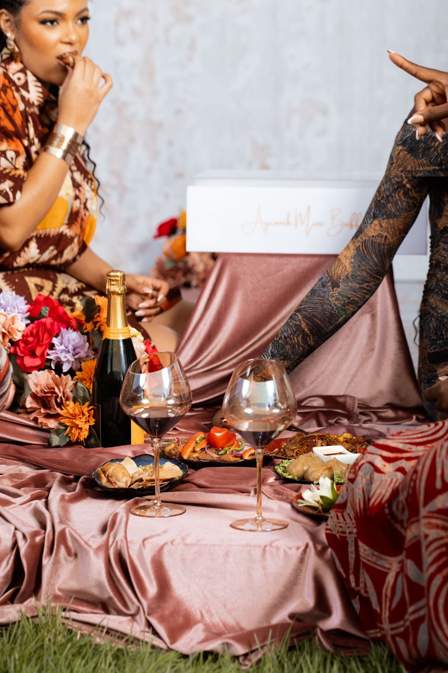 Elegant outdoor picnic setup with wine, flowers and appetizers on pink satin.