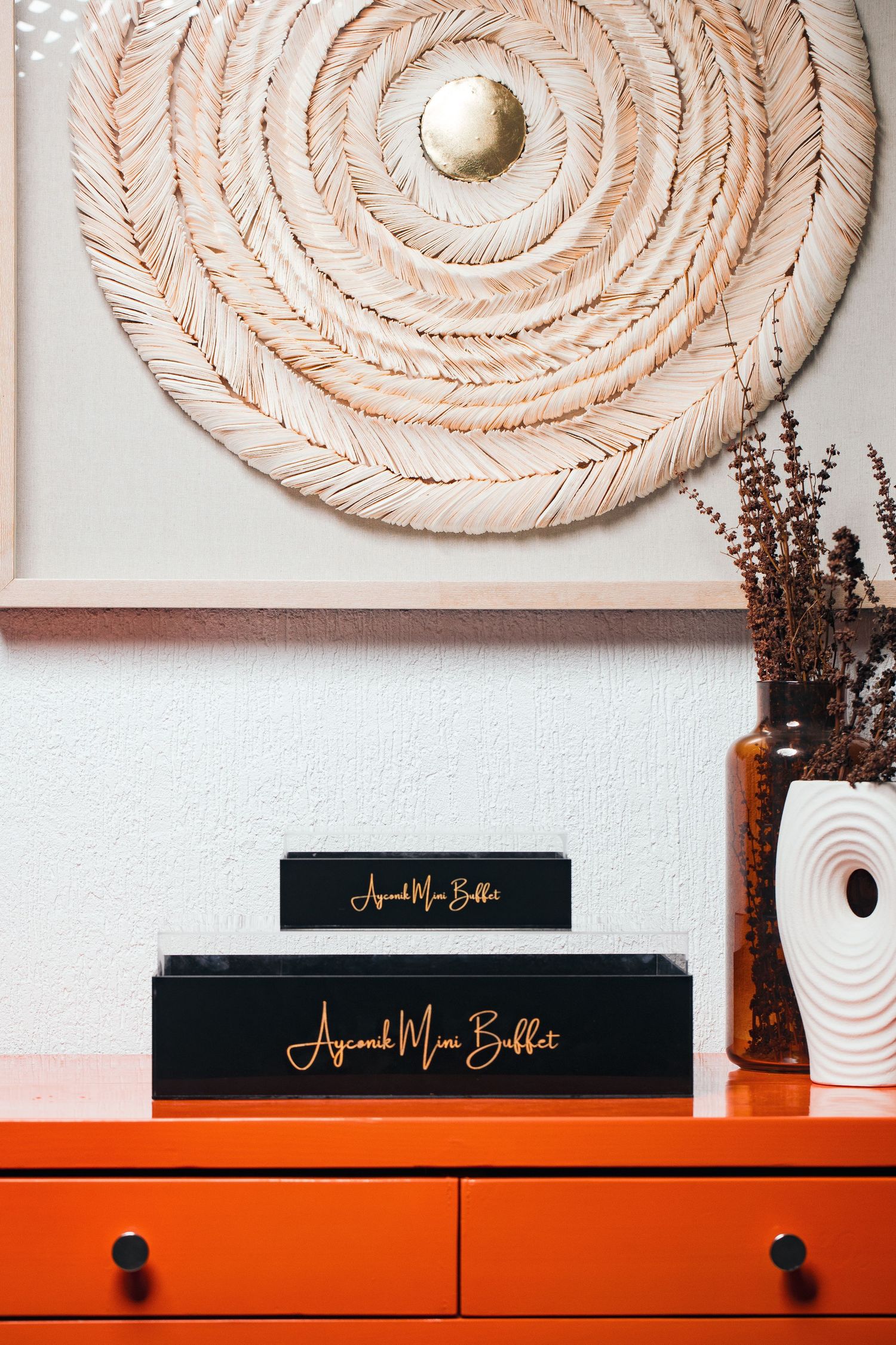 Decorative circular rope wall art above orange cabinet with black boxes.