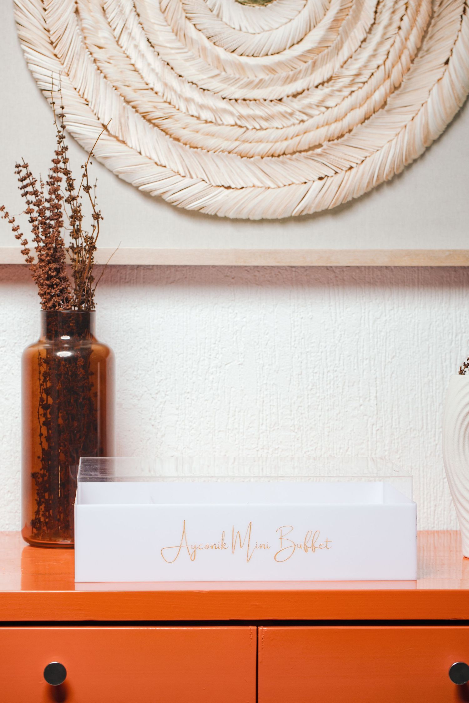 Clean minimalist product display with orange shelf and branded signage against white wall.