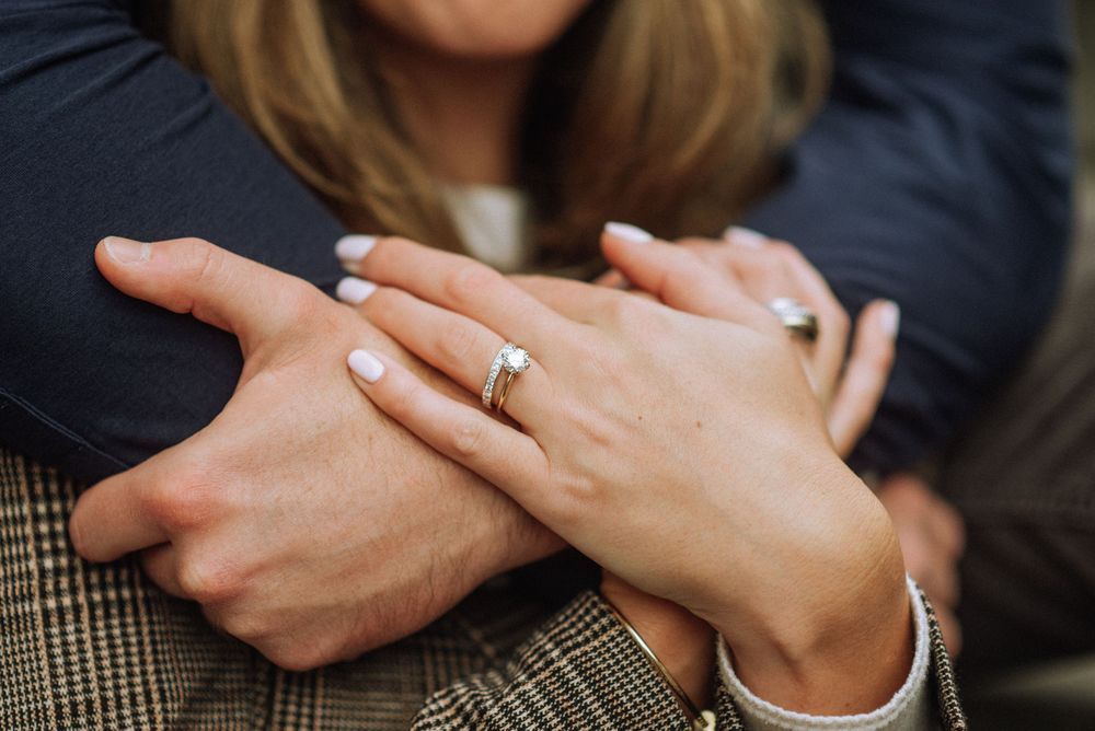 Close up of intertwined hands showing an engagement ring against a plaid fabric.