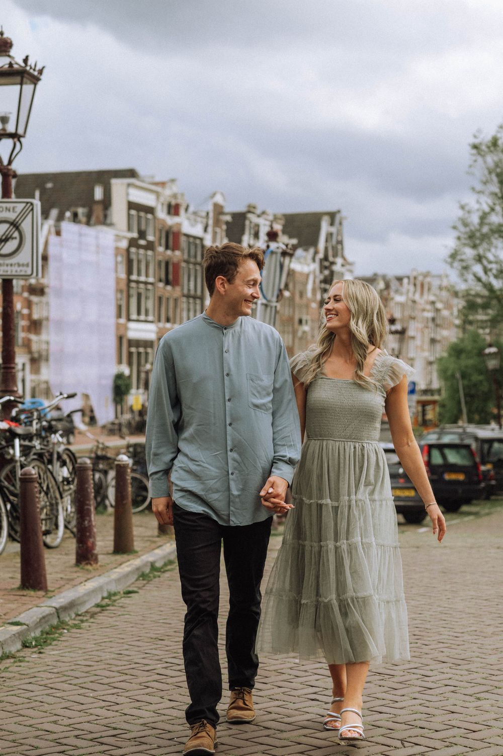Couple walking together on a cobblestone street in Amsterdam with historic buildings in background.