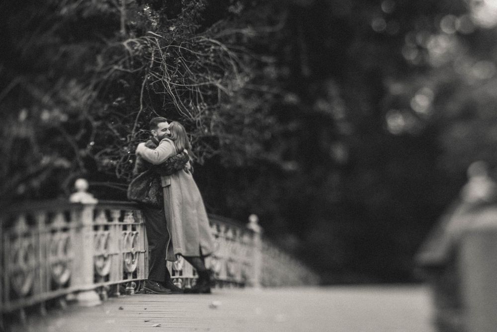 An artistic black and white photo of a couple embracing on a bridge.