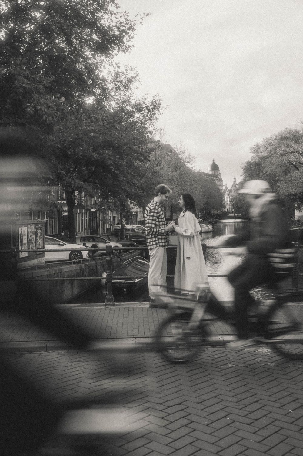 Black and white street scene with cyclists passing by in Amsterdam.