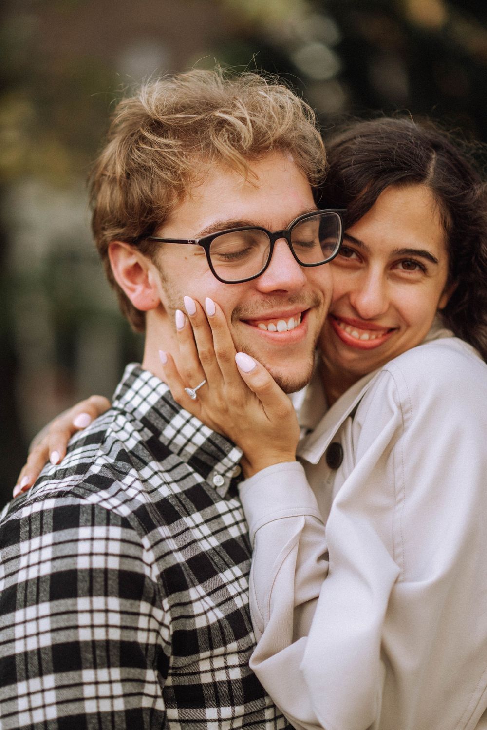 A romantic engagement photo shows a couple embracing and smiling with a sparkly ring visible.