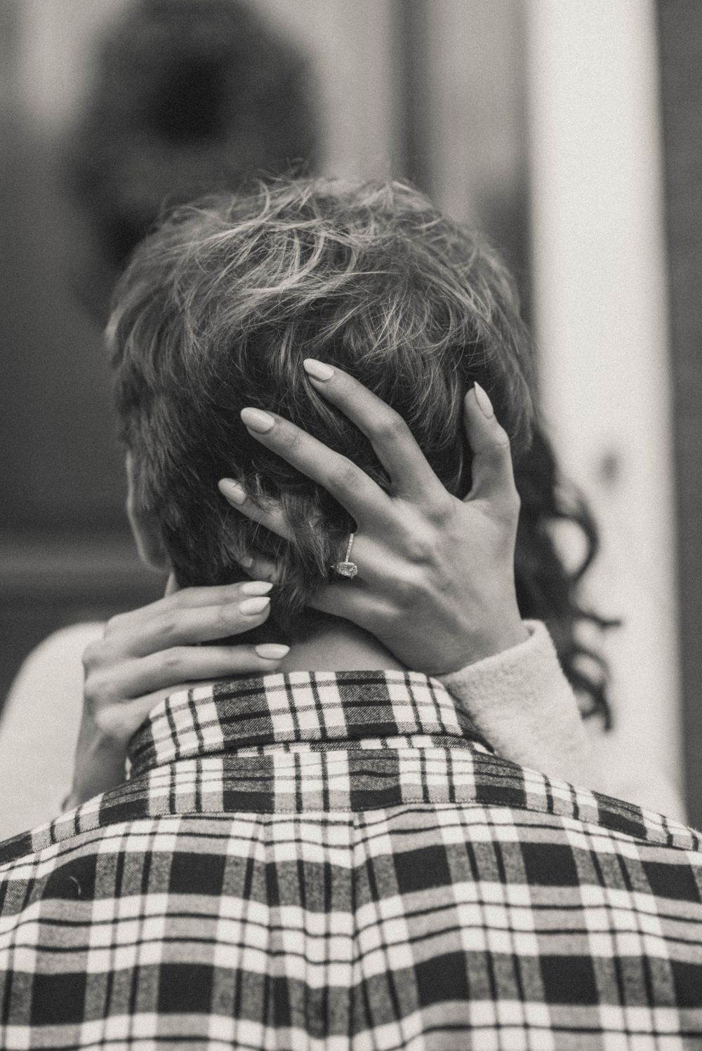 Close up of hands with manicured nails embracing from behind against a plaid shirt pattern.