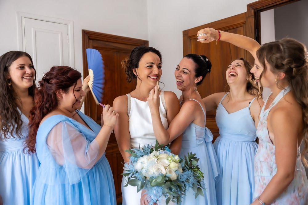 Bridesmaids in light blue dresses sharing joyful moments during wedding preparations.
