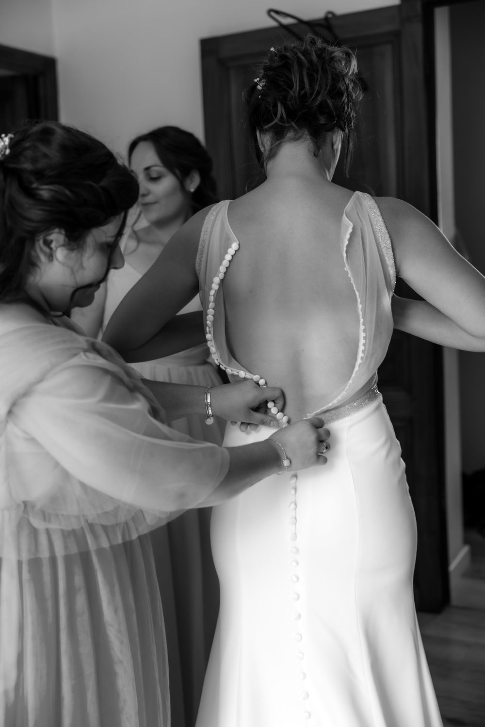 Helper assisting with white wedding dress buttons during preparation.