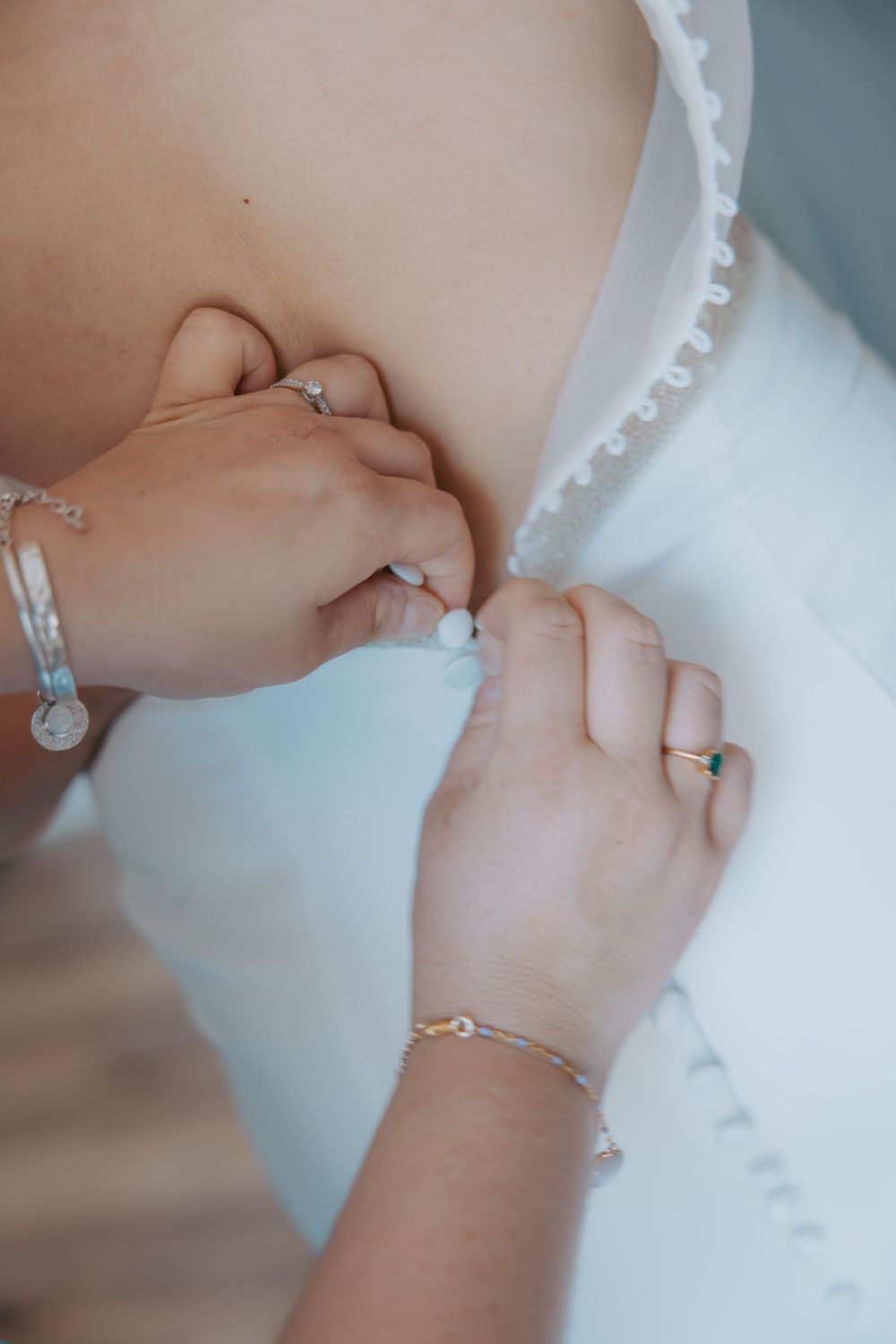 Close-up of delicate pearl buttons being fastened on a wedding dress.