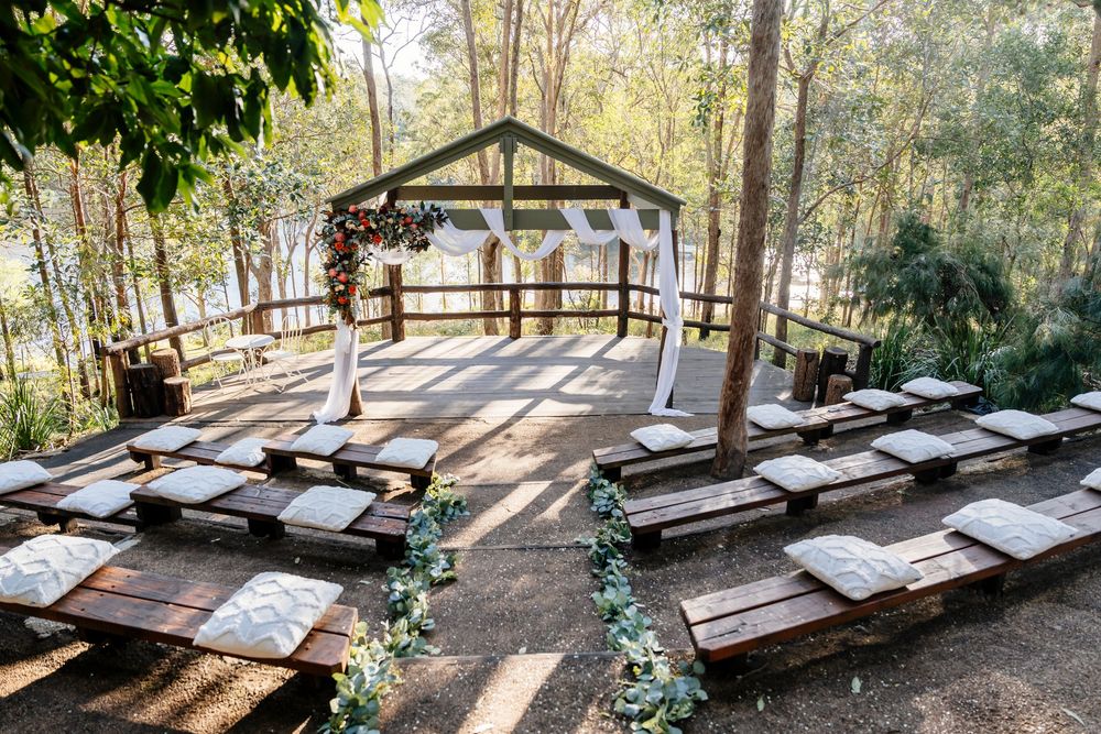 A row of rustic wooden lounge chairs line a covered outdoor deck overlooking a peaceful forest setting.