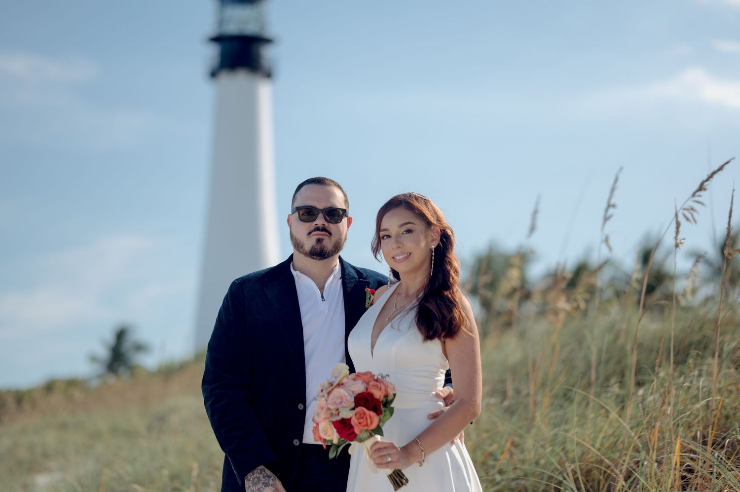 Newlywed couple shares romantic moments on a scenic hillside with tall grass and blue skies in the background.