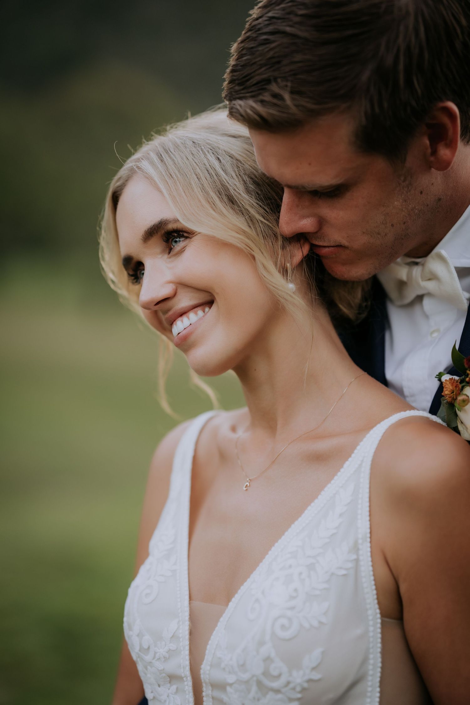 A romantic moment between newlyweds embracing outdoors, with the bride wearing a white lace dress.