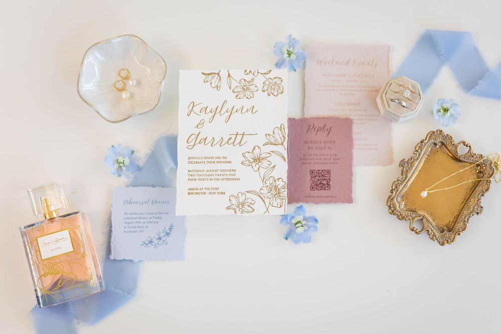Wedding invitation suite with blue accents, perfume bottle and vintage frames on white background.