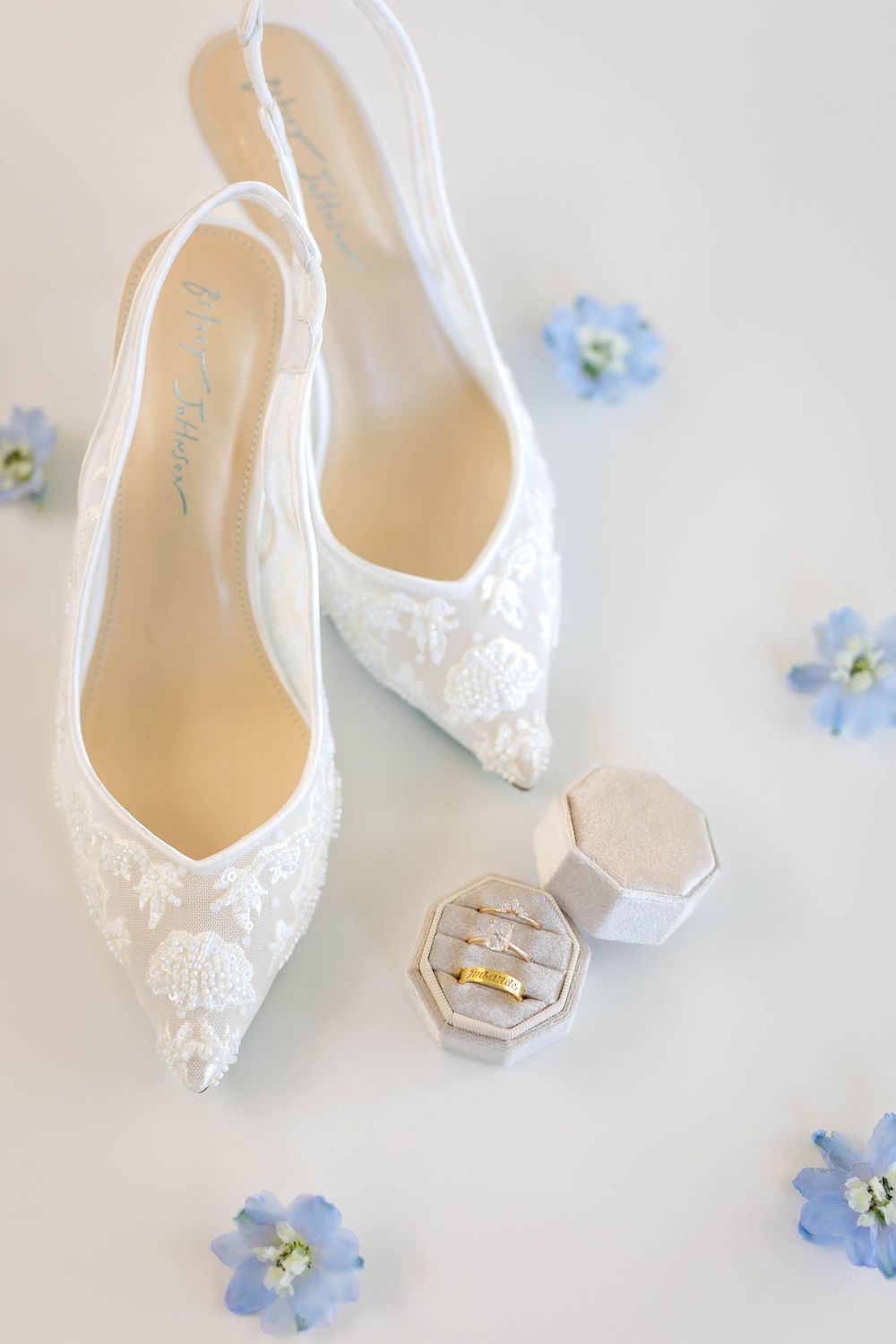 White lace bridal shoes and ring box decorated with light blue flowers on a white surface.