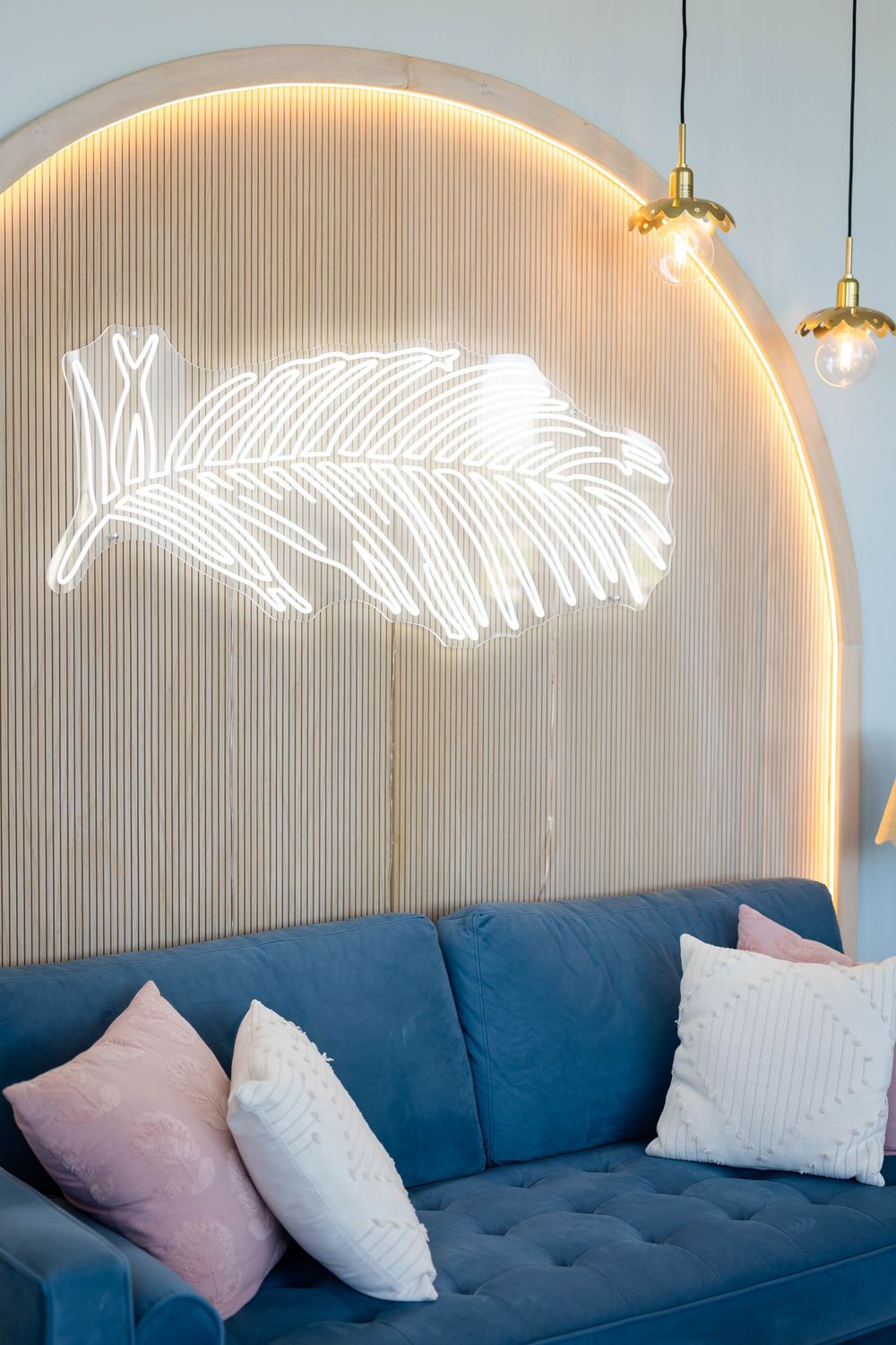 Modern interior features blue sofa beneath illuminated feather wall art.