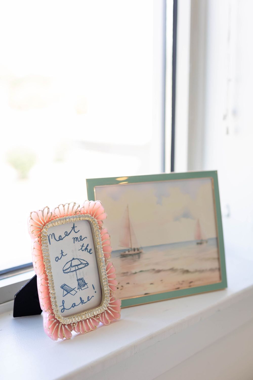 Vintage-style decorative frames with coral trim displayed on a white windowsill.