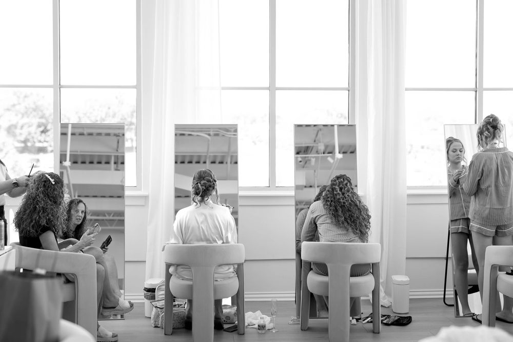 Black and white image of wedding preparations with people seated at a getting ready station.