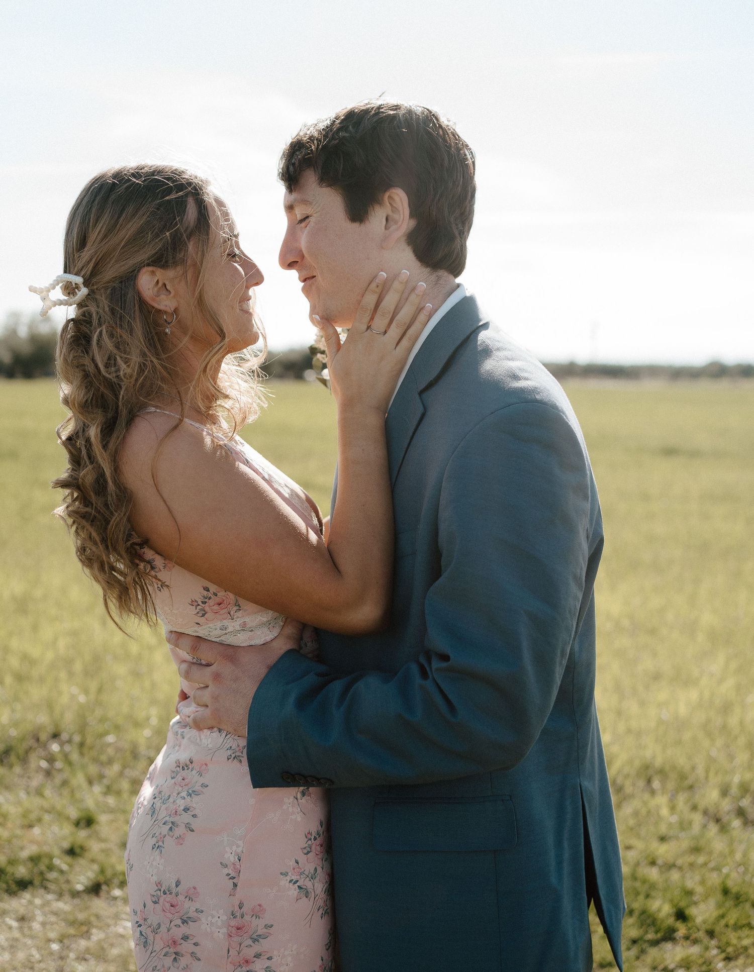 Couple in formal wear sharing a tender moment in an open green field.