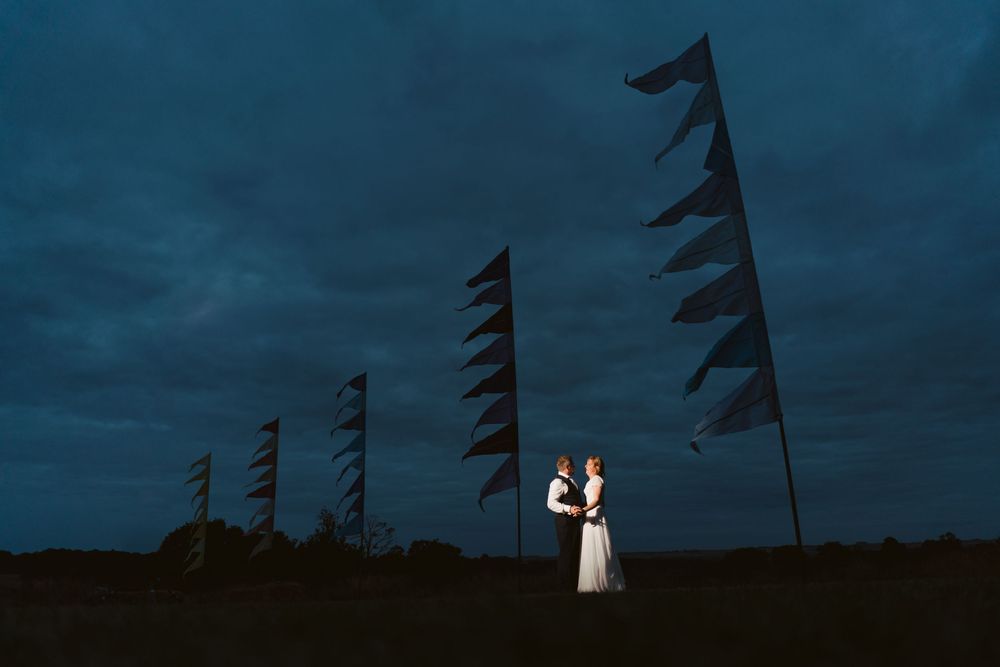 Bride and groom silhouetted against a night sky with flags at a Surrey wedding venue