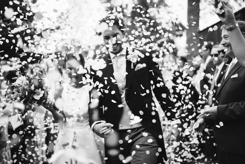 Joyful confetti moment outside the church in black and white wedding photography Surrey