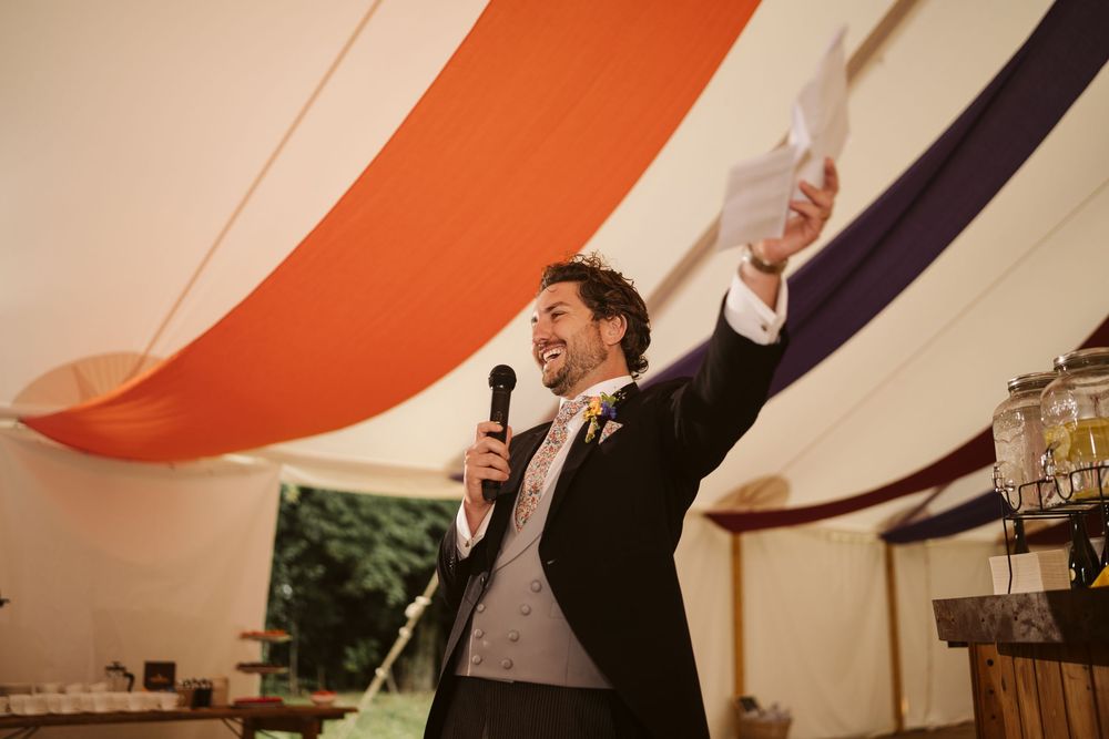 Best man delivering a speech inside a colourful big top marquee at a Surrey wedding
