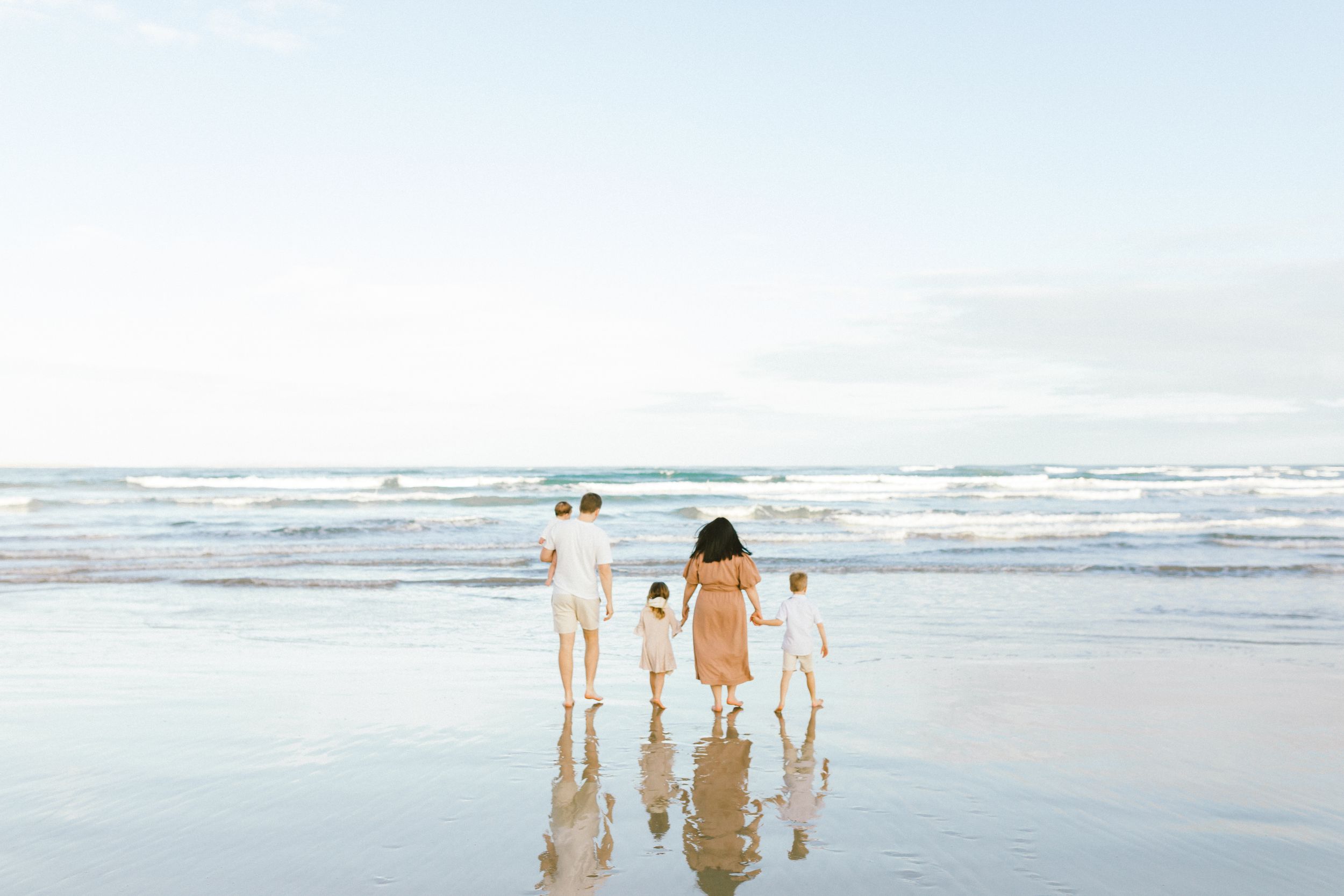 A group of people walk together along a misty beach shoreline at sunset with waves crashing in the background.