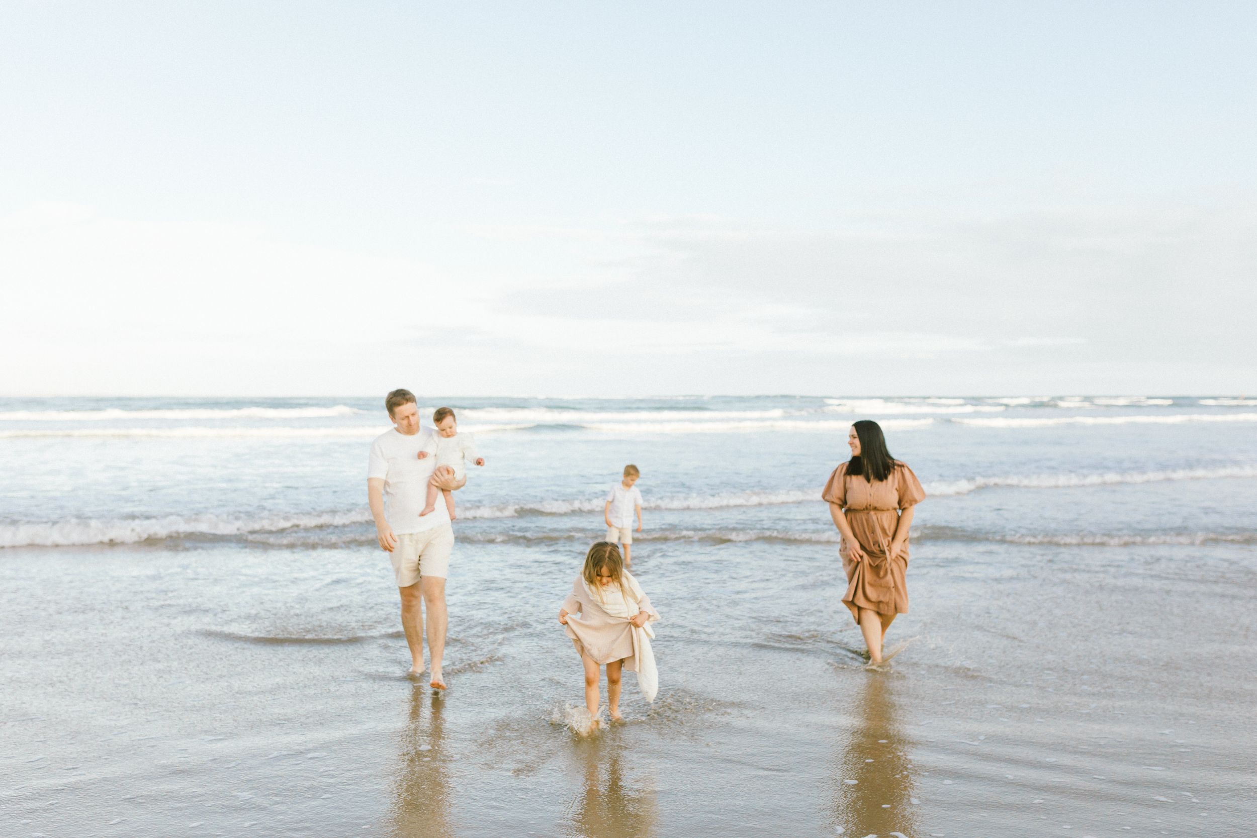 People walk together along the shoreline of a beach as waves crash against the sand on a sunny day.