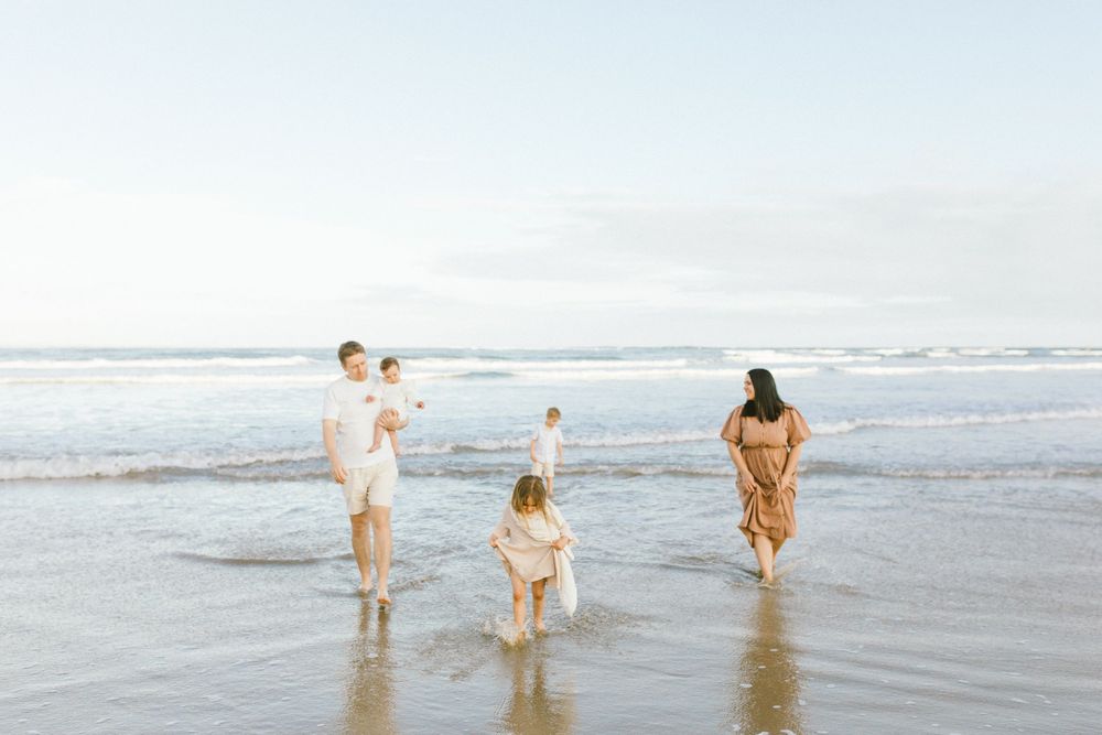 People walk together along the shoreline of a beach as waves crash against the sand on a sunny day.