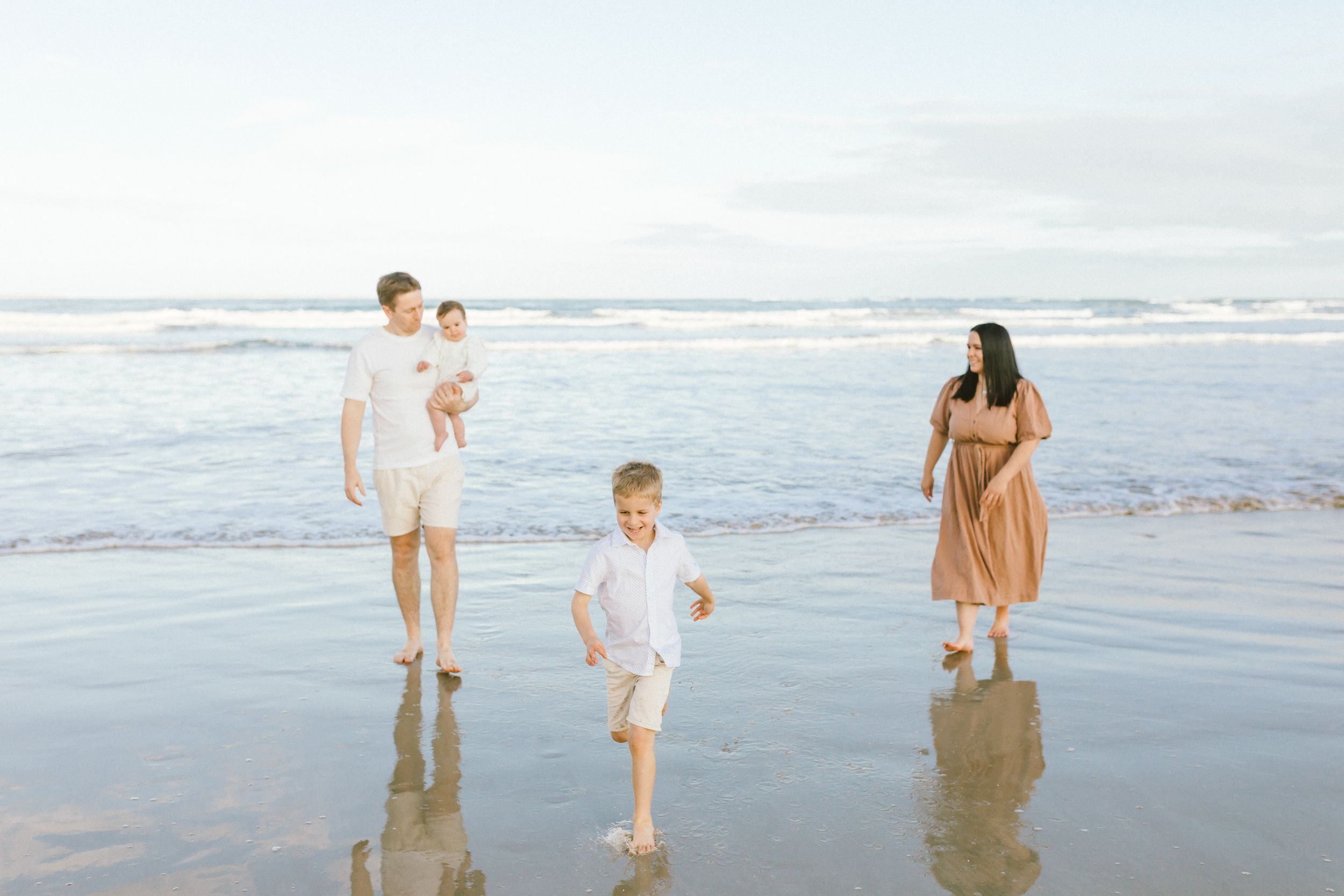 Group walking and playing together on a misty beach at sunset with waves and reflections in wet sand.
