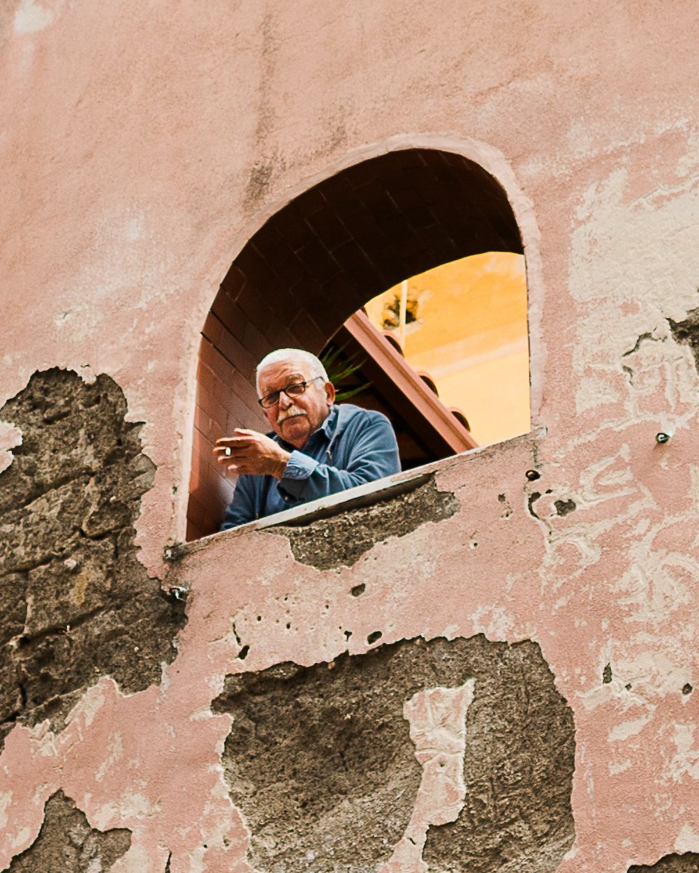 Procida Pink building with an older man leaning out of an arched open terrace smoking a cigarette.