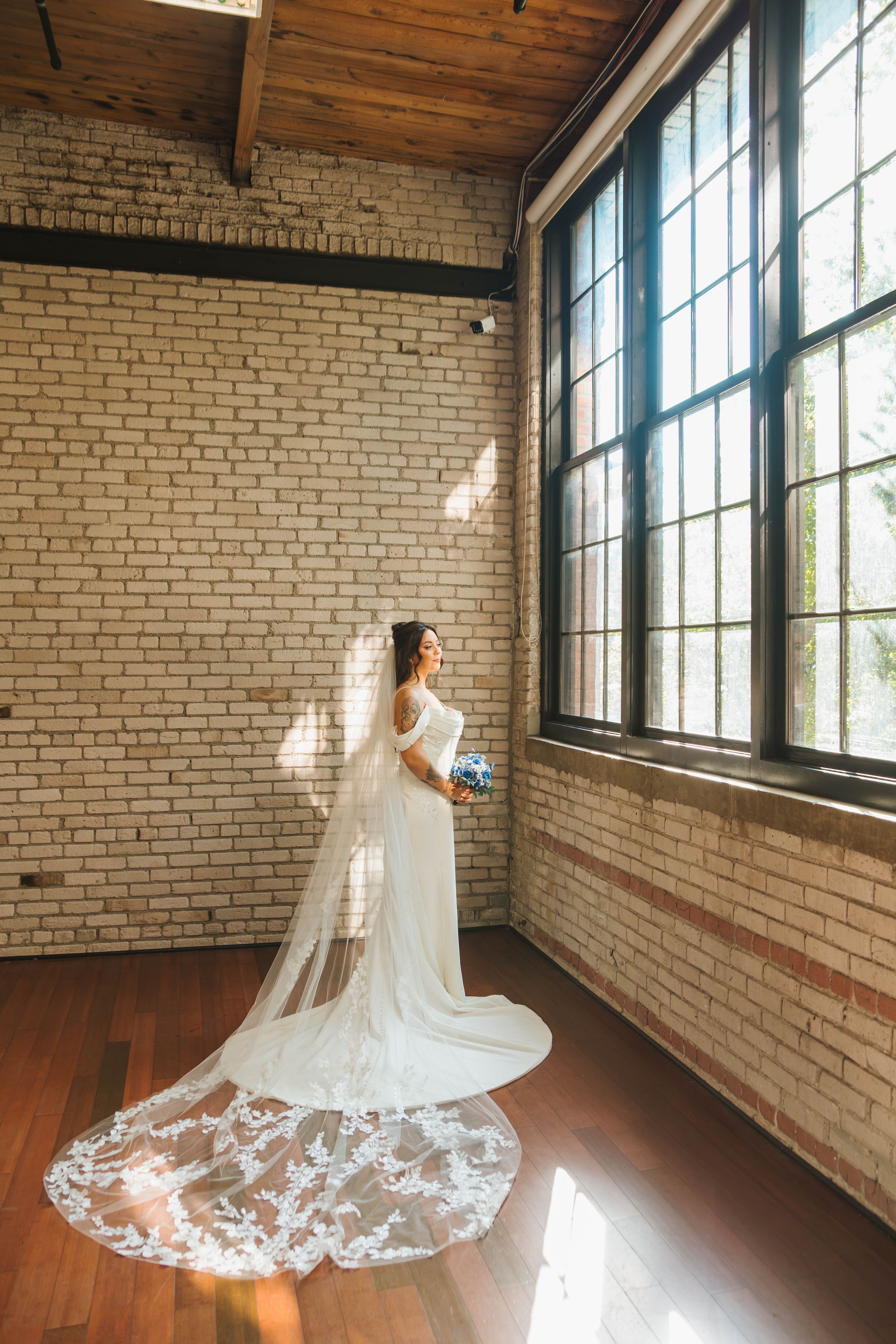 Elegant bridal portrait in a rustic brick loft with flowing white veil and natural window light.