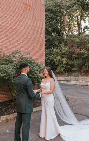 A couple shares a romantic moment in front of a brick wall, with the bride wearing a flowing white gown and long veil.