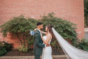 Newlywed couple shares romantic moments in front of a brick wall with cascading ivy during their wedding celebration.