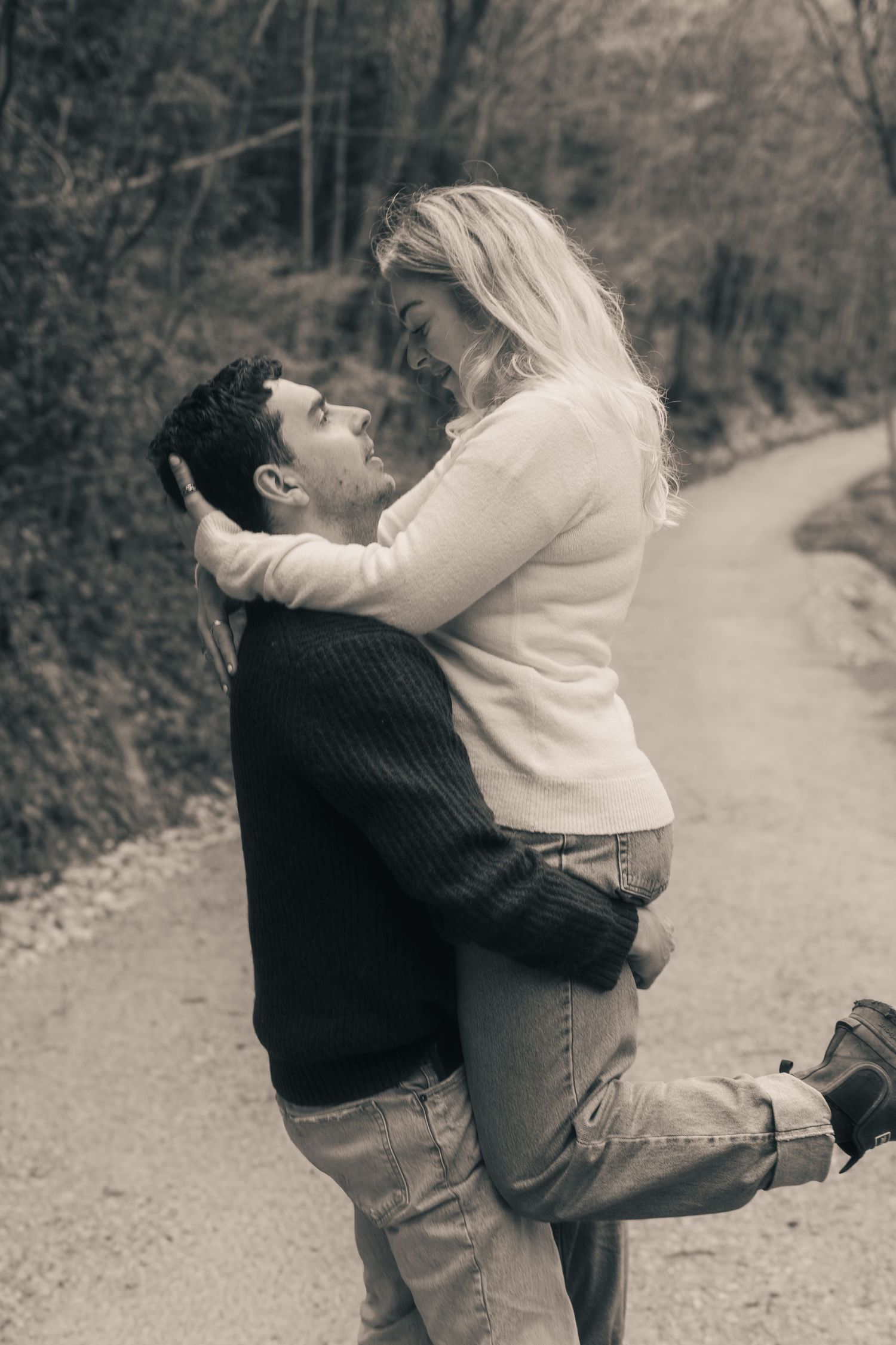 Romantic couple embracing on forest path, man lifting woman in sepia-toned portrait.