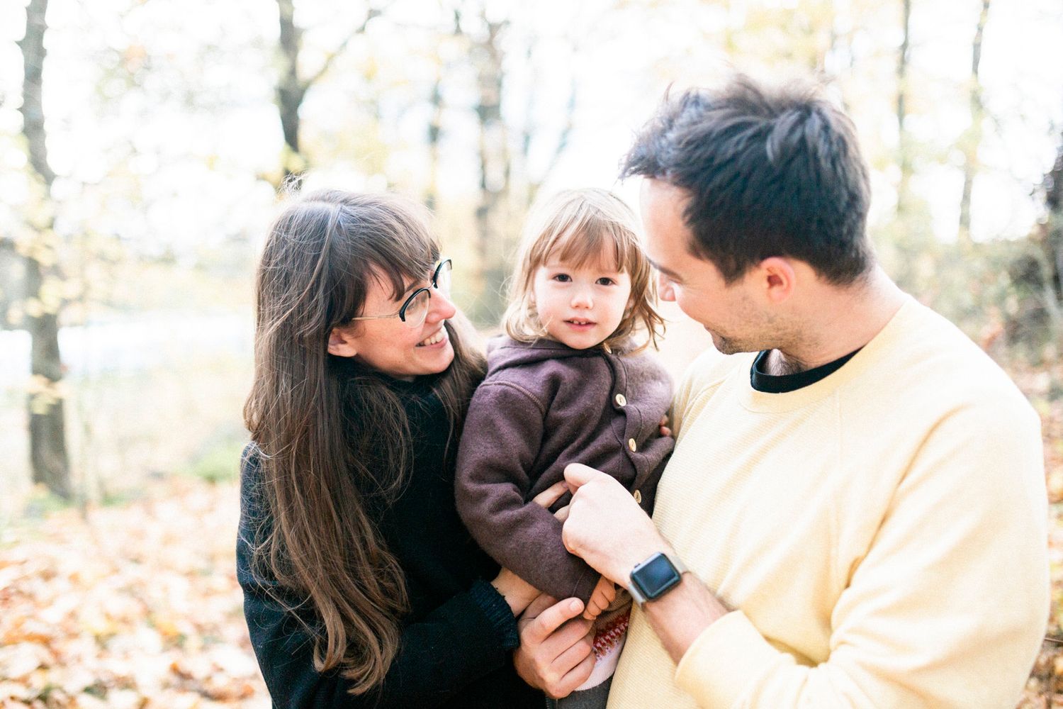 A casual autumn family moment captured among fallen leaves in the woods.