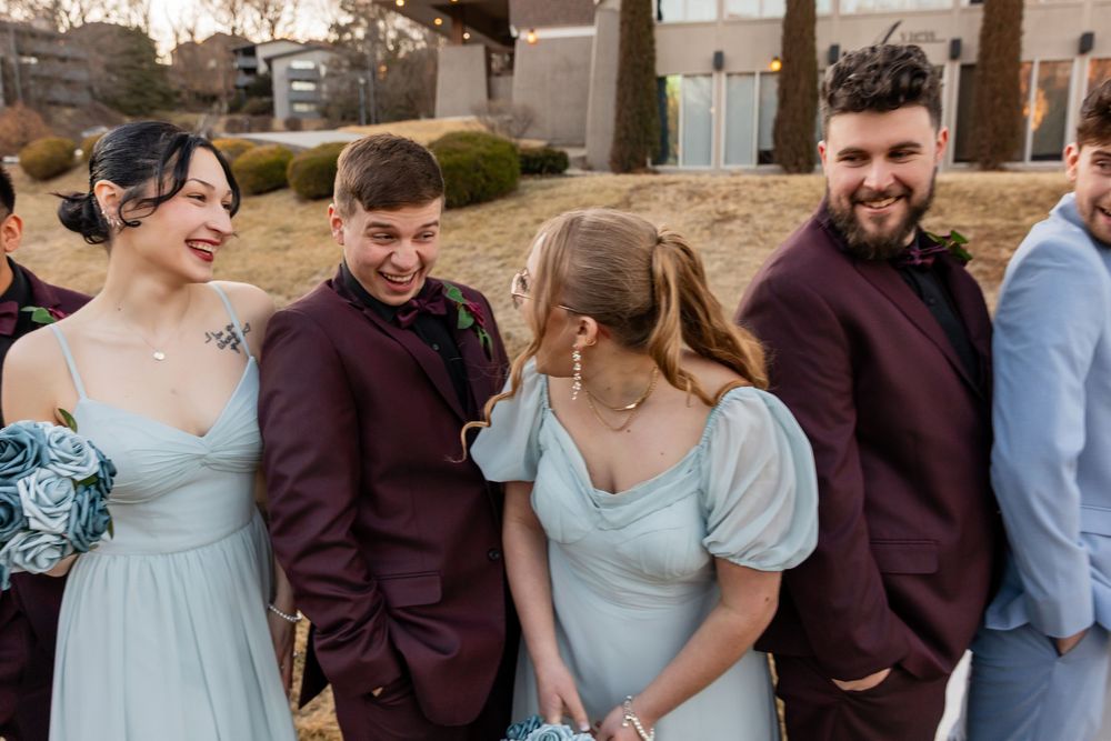 Wedding party in burgundy suits and blue dresses laughing together outdoors at a winter wedding celebration.