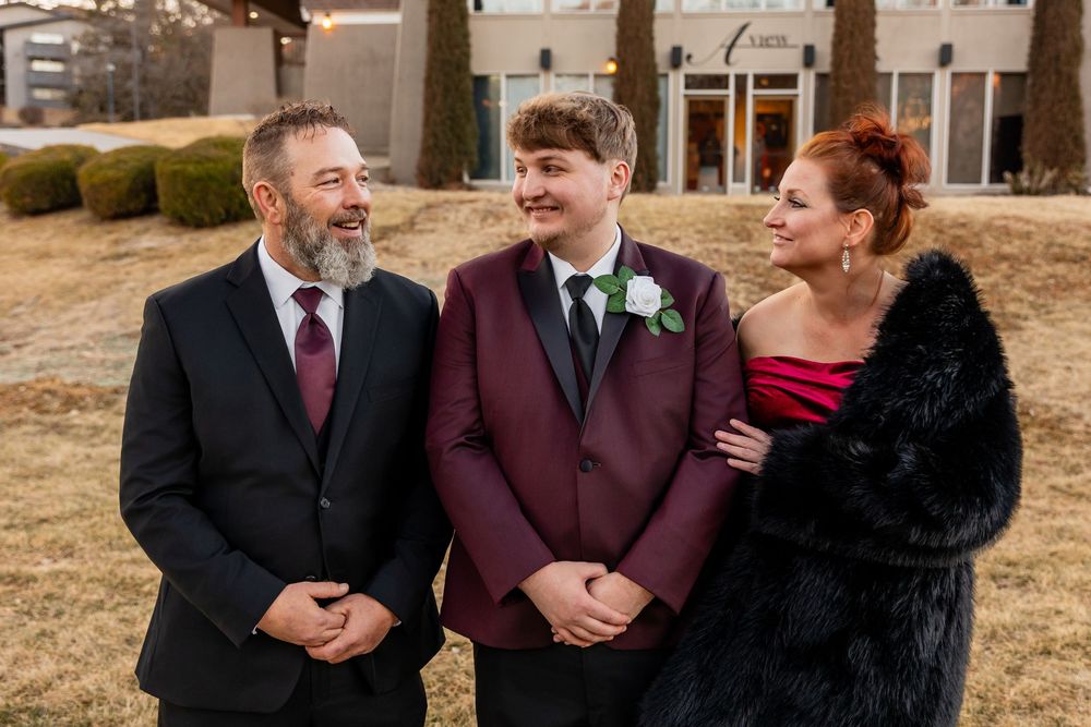 Family portrait at winter wedding with groom in burgundy suit flanked by parents in formal attire outdoors.